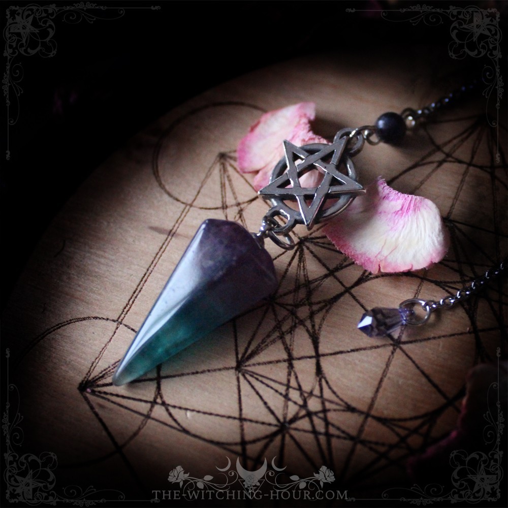 Pendule divinatoire en fluorite, monture pentacle, posé sur une planche de géométrie sacrée